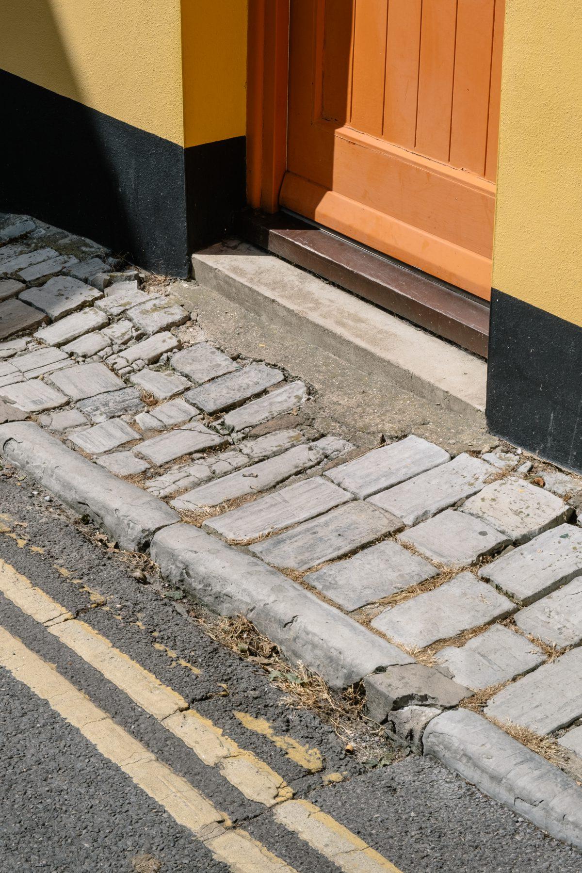 A photograph showing a detailed view of a cobbled street, colourful door and building exterior in Lyme Regis, Dorset.