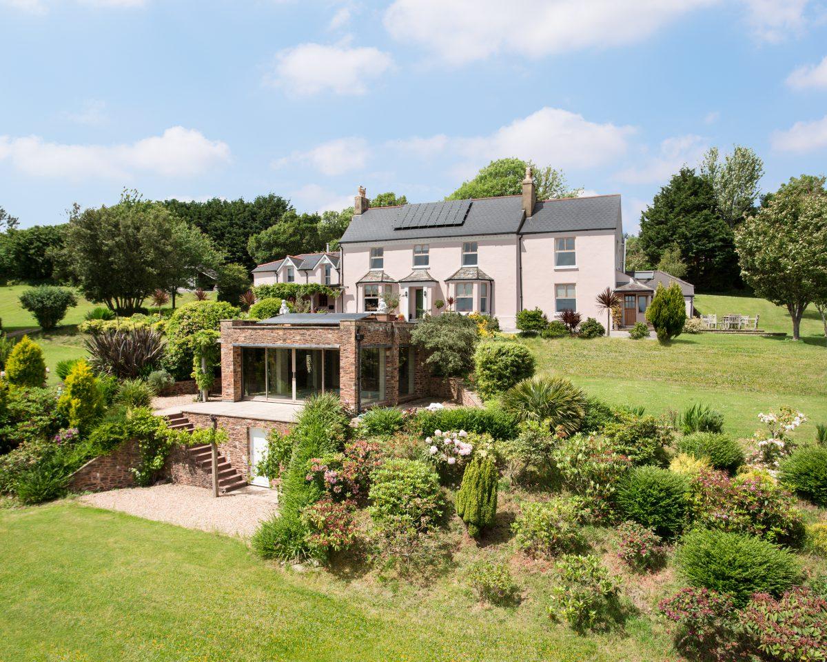 Elevated photograp of a waterside property surrounded by gardens and with a separate pool house. Located in Corwall.