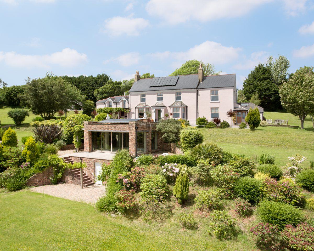 Elevated photograph of a waterside property surrounded by gardens and with a separate pool house. Located in Cornwall.