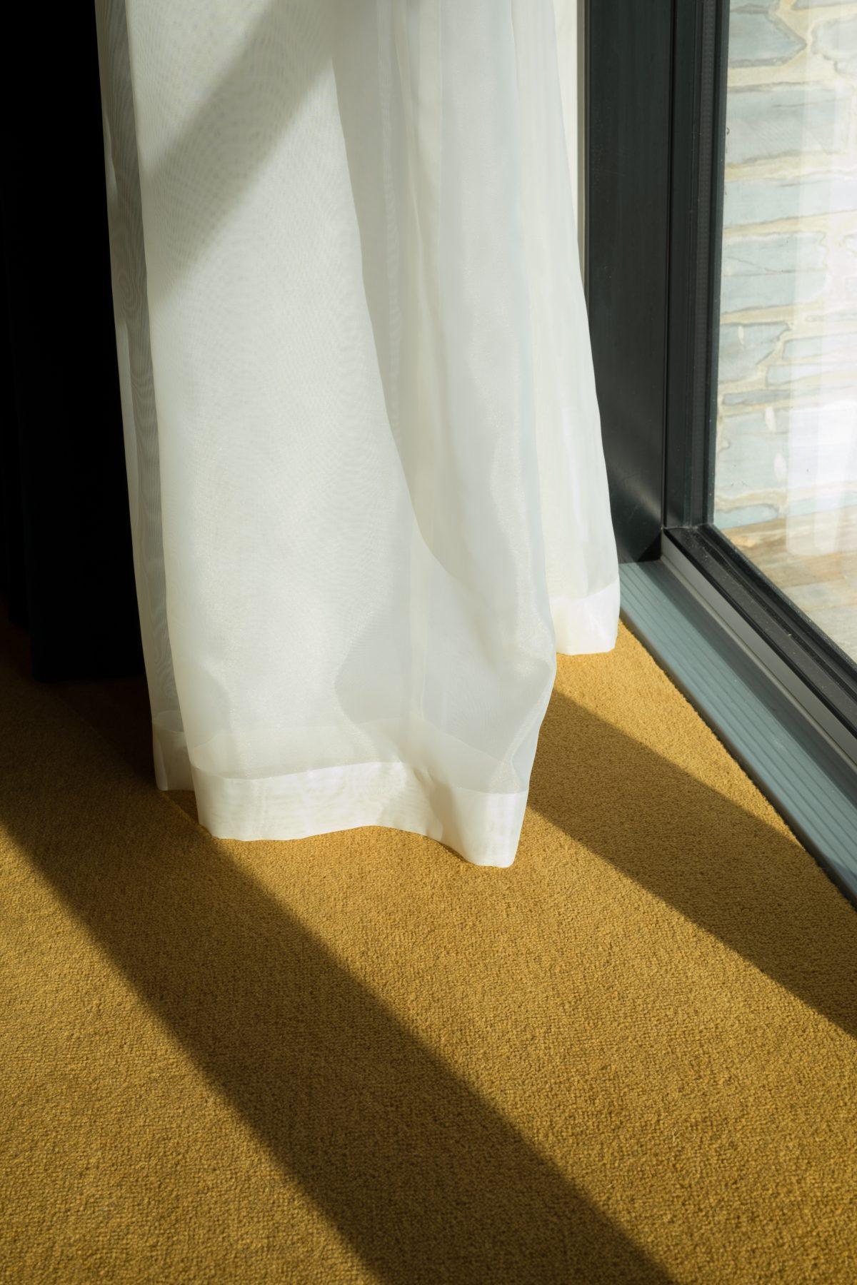 Detailed view of a curtain. Strong light is casting a shadow across the carpet. At a location in Cornwall.